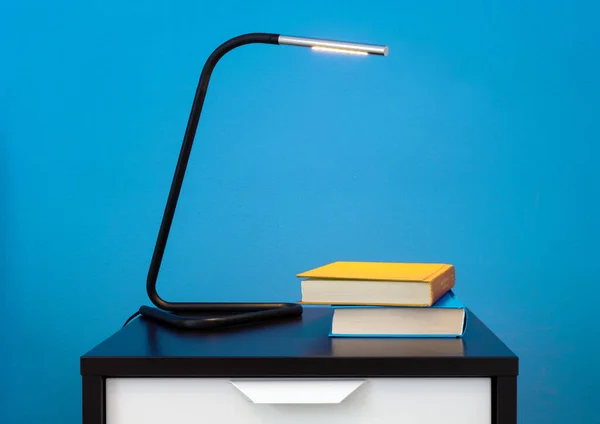 一盏现代灯 两本书放在床头柜上 靠着一面蓝色的内墙 — 图库照片