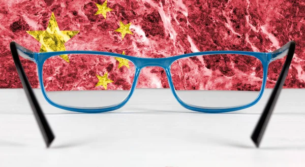 Creative flag of China seen through a pair of eyeglasses lying on a white table