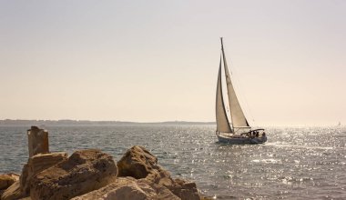 Günbatımında kayalık bir sahilden seyreden yelkenli.