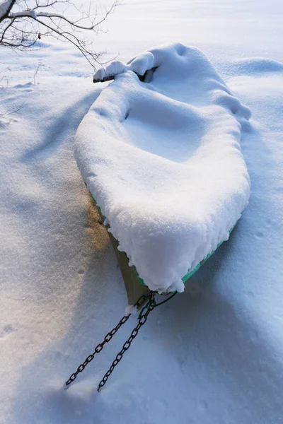 Rowboat lie in snow on the shore of an ice-covered frozen river — 스톡 사진