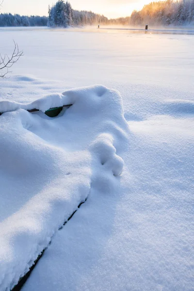 Roddbåt ligger i snö på stranden av en istäckt frusen flod — Stockfoto