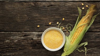 Polenta mısır ezmesi ahşap bir masada porselen bir kase. Mısır kulakları ve mısır parçaları kaselerin yanında. Glütensiz sağlıklı beslenme