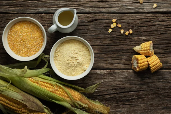 Corn oil, polenta corn grits, corn flour in a porcelain bowl on a wooden table. Ears of corn and slices of corn next to bowls. Gluten free healthy foods.