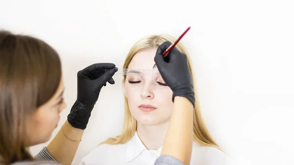 Female cosmetologist performs eyebrow correction on beautiful models in the beauty parlor. The girl's face is a blonde. Close-up. Facial care — Stock Photo, Image