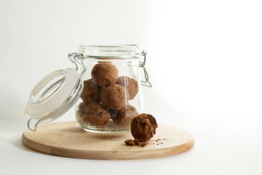 Cam kavanozdaki enerji topları. Tabaklar beyaz arka planda ahşap bir standın üzerinde. Kakao tozunda tatlı atıştırmalık