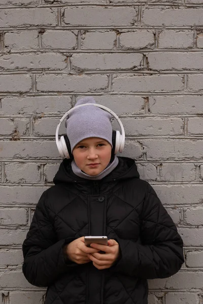 Un adolescente escucha música en los auriculares y sostiene un teléfono —  Fotos de Stock