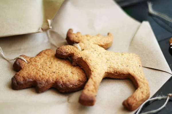 Frohe Weihnachten. Lebkuchen und ein stilvolles rustikales Weihnachtsgeschenk in Kraftverpackung auf schwarzem Hintergrund. umweltfreundliche Weihnachtsdekoration mit Bindfäden. Handarbeit mit Kindern. Handgemachtes Geschenk — Stockfoto