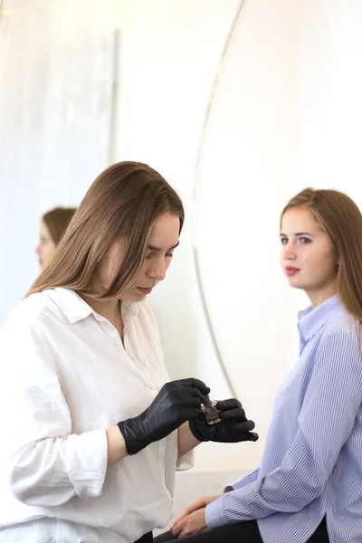 Female cosmetologist performs eyebrow correction on beautiful models in the beauty parlor. Fair-haired girl. Close-up. Facial care — Stock Photo, Image