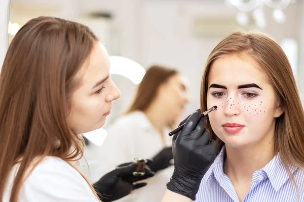 Uma cosmetologista feminina realiza correção de sobrancelha em um belo modelo em um salão de beleza. Aplicando sardas no rosto, cuidados com a pele e tratamentos de salão. Modelo com pigmentação vitiligo. Tintura segura — Fotografia de Stock