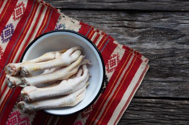 Tavuk bacakları ahşap bir masada bir kasenin içinde yatıyor. Tabağın altındaki kırmızı mutfak peçetesi. Diyet ve sağlıklı beslenme için yararlı organik ürün. Jöle için hammadde