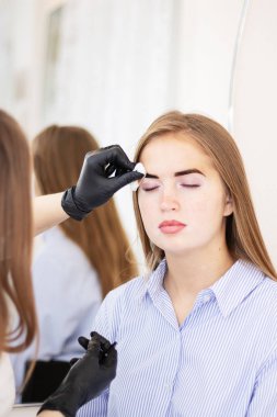 Kadın bir kozmetikçi güzellik salonunda güzel bir model üzerinde kaş düzeltmesi yapıyor. Kahverengi saçlı kız, yakın plan. Yüz ve kuaför tedavileri. Vitiligo pigmentasyonu olan bir model. Güvenli boyama.