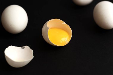 Beyaz yumurtalar siyah arkaplana saçılmış. Bir yumurta kırıldı ve yumurta sarısı görünür durumda. Minimalist tasarım ve renk eğilimi 2020. Üst görünüm.