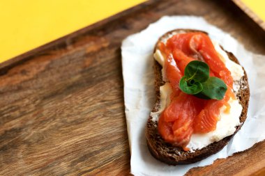 Kahvaltı yoğun bir günde başlar. Somon balıklı sandviç ve mevsimlik otlar. Sağlıklı beslenme konsepti. Sarı arka planda aperatif tepsisi