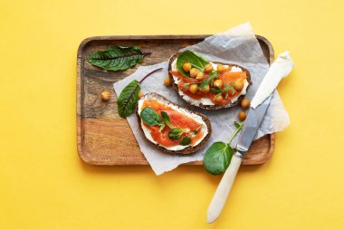 Kahvaltı hareketli bir gün başlatır. Hafif tuzlu somonlu sandviç, nohut ve mevsimlik otlar. Sağlıklı beslenme konsepti. Tepside bir aperatif ve tereyağlı bir bıçak var, parlak sarı bir arka plan.