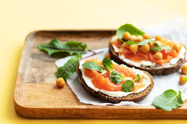 Breakfast starts a brisk day. Sandwich with slightly salted salmon, chickpeas and seasonal herbs. Healthy eating concept. On the tray is a snack and a knife with butter, a bright yellow background