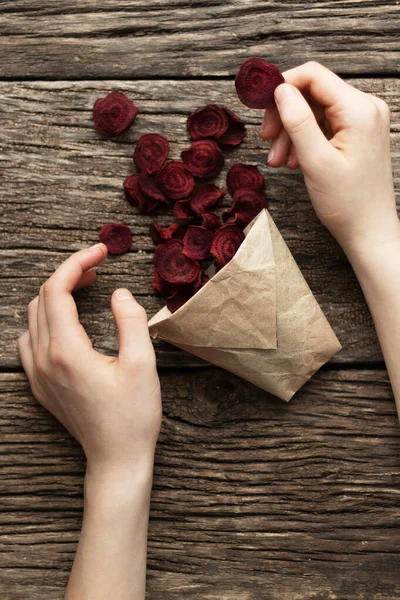 Home-made beet chips. Snacks are wrapped in a paper bag. Hand holds food bag. Handmade healthy vegetables chips — Stock Photo, Image