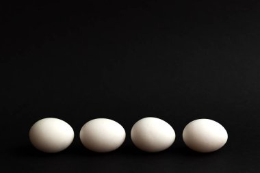 Siyah arka planda dört beyaz yumurta. Minimalizm. Paskalya, kavramsal tasarım. Üst görünüm