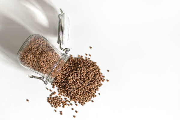 A glass jar lies on the table. Red lentils spilled out of it. Food stocks for future use. Safe and environmentally friendly food storage. Minimalism in the design of space.