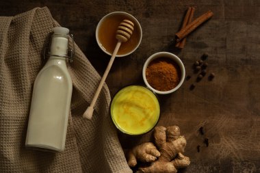 Zerdeçal sütü bardağa dökülür. Yanında içki yapmak için gereken malzemeler var. Peçetedeki süt, baharat ve bal. Karanlık huysuz arka planda altın içecek, seçici odaklanma. Üst