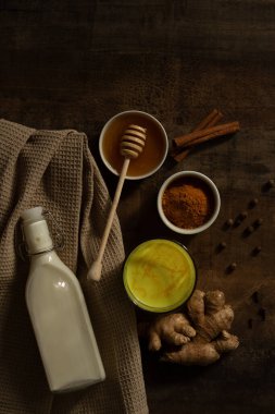 Zerdeçal sütü bardağa dökülür. Yanında içki yapmak için gereken malzemeler var. Peçetedeki süt, baharat ve bal. Karanlık huysuz arka planda altın içecek, seçici odaklanma. Üst