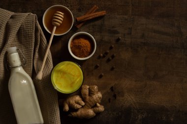 Zerdeçal sütü bardağa dökülür. Yanında içki yapmak için gereken malzemeler var. Peçetedeki süt, baharat ve bal. Karanlık huysuz arka planda altın içecek, seçici odaklanma. Üst