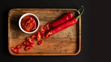 Sos kabına Harissa sosu. Pişirmek için gerekenler: Biber, sarımsak ve baharat. Her şey ahşap bir tepside yatıyor. Siyah arkaplan ve üst görünüm.