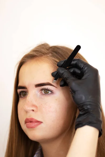 A female cosmetologist performs eyebrow correction on a beautiful model in a beauty salon. Girl with brown hair close-up. Facial and salon treatments. Model with vitiligo pigmentation. Safe tinting eyebrows with henna.