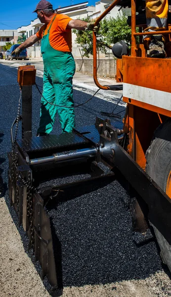 Trabalhadores em uma máquina de paver controlar a elaboração de uma nova camada de asfalto — Fotografia de Stock