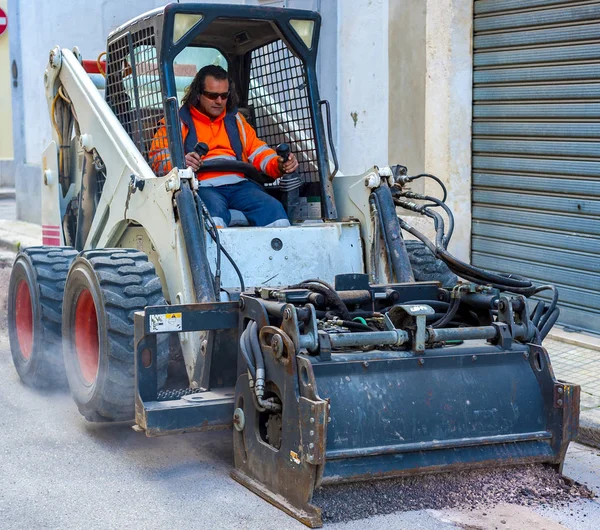 Arbetaren driver kompaktlastare bort sliten asfalt — Stockfoto