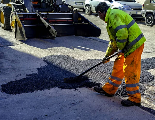 worker leveling fresh asphalt during asphalt pavement repair or construction works