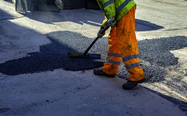 worker leveling fresh asphalt during asphalt pavement repair or construction works
