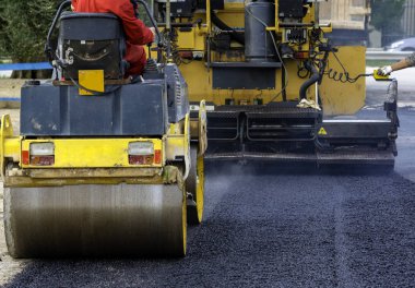 İşçi, asfaltı sıkıştırmak için titreşen yol silindirine önderlik ediyor.