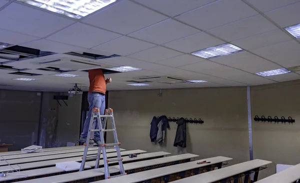 Worker repairing board ceiling with gypsum. In the classroom