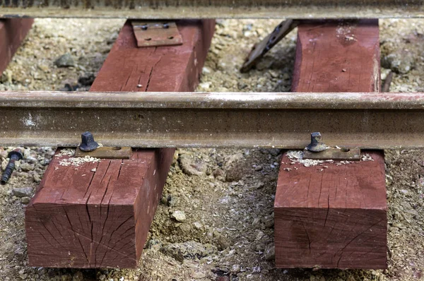 Bolted butt of rails and wooden sleepers laid on groundwork crushed stone. The sleepers have a red color because they have been impregnated with iron oxide — Stock Photo, Image