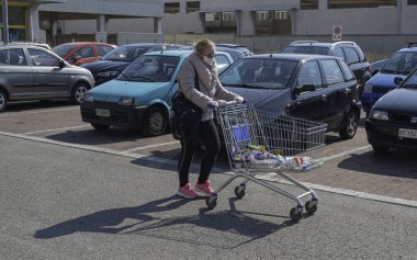 Modugno, İtalya - 4 Nisan 20: Maskeli ve lastik eldivenli kadın, Corona karşıtı tedbirler sonucunda, alışveriş sonrası boş otoparkta yürüyor