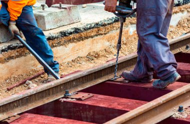 Rayları sürgüleyen demiryolu işçileri. Hafif portatif sondaj makinesi olan detaycı.