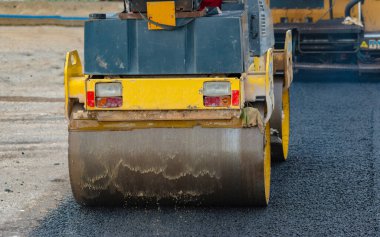 İşçi, asfaltı sıkıştırmak için titreşen yol silindirine önderlik ediyor.