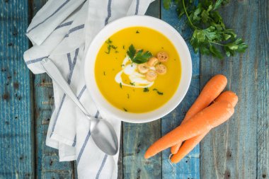 Krem ve ahşap zemin üzerine maydanoz ile havuç çorbası