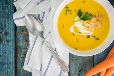 Krem ve ahşap zemin üzerine maydanoz ile havuç çorbası