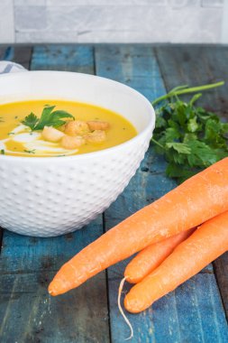 Krem ve ahşap zemin üzerine maydanoz ile havuç çorbası