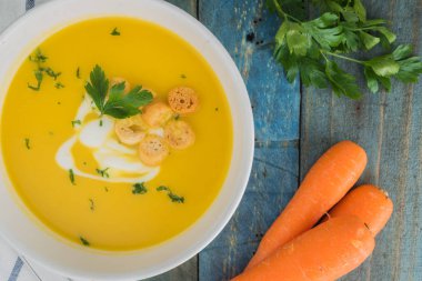 Krem ve ahşap zemin üzerine maydanoz ile havuç çorbası