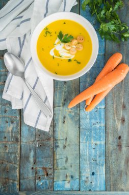 Krem ve ahşap zemin üzerine maydanoz ile havuç çorbası