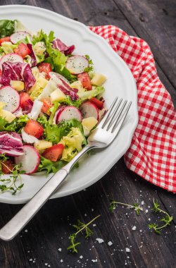 Karışık yeşillik, turp, peynir ve domates ahşap arka plan üzerine bir tabak içinde taze salata. İtalyan Akdeniz veya Yunan mutfağı. Vejetaryen vegan gıda