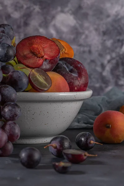 Плоди Натюрморт з фруктами на сковороді. Бетонна стіна. Драматичне світло. Виноград, абрикоси та сливи . — стокове фото