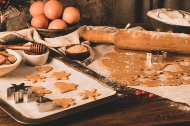 Zencefilli kurabiye yapıyorum. Çiğ hamur, zencefilli çörek adam, noel ağacı, yıldız, kırsal masada kağıt üzerinde kar taneleri merdaneli iğne. Pişirme için hazırlanılıyor
