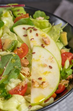 Salata. Bahar sebze salatası. Domatesli, elmalı, fındıklı, tohumlu ve limonlu taze sebze salatası. Salata kasesine zeytin yağı dökülüyor.