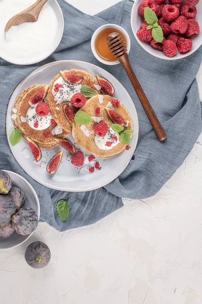 Pancakes with raspberries, figs, yogurt, coconut zest, honey and mint leaves on a plate