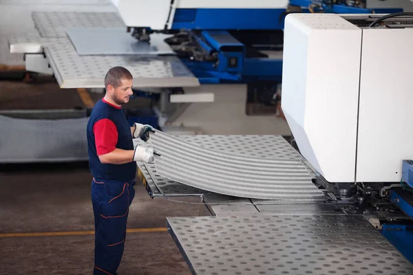 Dentro de una fábrica, trabajador industrial en acción en la máquina de la prensa del metal que sostiene un pedazo de acero listo para ser trabajado . — Foto de Stock