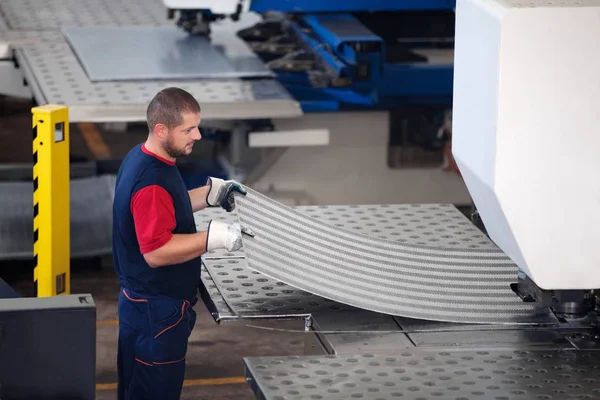 Dentro de una fábrica, trabajador industrial en acción en la máquina de la prensa del metal que sostiene un pedazo de acero listo para ser trabajado . — Foto de Stock