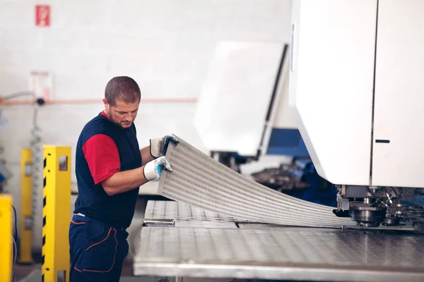 Dentro de una fábrica, trabajador industrial en acción en la máquina de la prensa del metal que sostiene un pedazo de acero listo para ser trabajado . — Foto de Stock